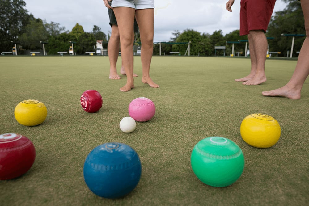 Colourful bowls and a jack on the green, with barefoot players standing behind